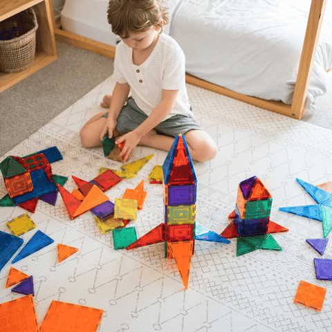 Child building a TileTek magnetic tile rocket on the floor beside loose tile pieces