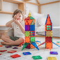 Child sitting beside TileTek magnetic tile rocket towers, reaching for a small tile