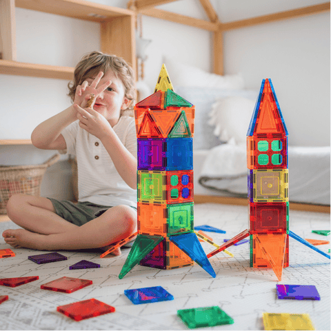 Child sitting beside TileTek magnetic tile rocket towers, reaching for a small tile