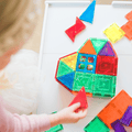 Child pressing a red triangle tile into a TileTek magnetic tile rocket build