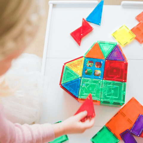 Child pressing a red triangle tile into a TileTek magnetic tile rocket build