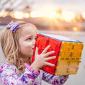 Child holding a red and yellow TileTek large square tile cube outdoors at sunset