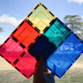 Child holding red, yellow, teal and blue TileTek large square tiles against the sky