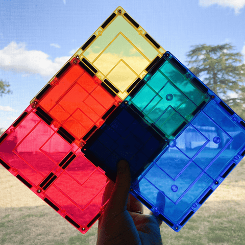 Child holding red, yellow, teal and blue TileTek large square tiles against the sky