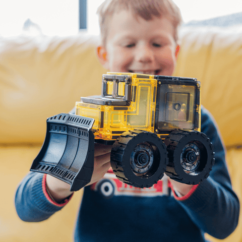 Child holding an assembled magnetic tile bulldozer with oversized wheels