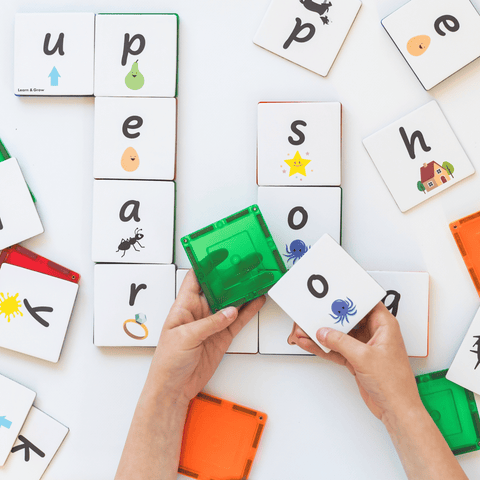 Hands connecting magnetic tiles topped with Tile Tek lower-case letter toppers