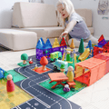 Child reaching into a magnetic tile village scene with peg dolls and curved road toppers
