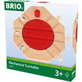 A Brio World Mechanical Turntable in its packaging. This turntable, by Brio, features a vibrant red circular center and natural wood-colored edges, making it the perfect addition to your BRIO World railway set. The green and white packaging indicates it is suitable for ages 3 and up.