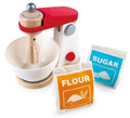 The Hape Mix & Bake Blender by Hape is a high-quality wooden toy kitchen mixer with a red handle and white base, featuring a wooden mixing arm and bowl. In front of it are two fabric sacks labeled "FLOUR" in orange and "SUGAR" in blue, both adorned with ingredient illustrations to ignite a child's imagination.