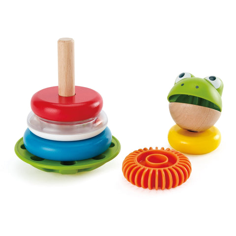 A photo showcasing colorful wooden toddler toys, featuring the Hape Mr. Frog Stacking Rings by HAPE with vibrant stacking rings in red, white, blue, and green on a vertical wooden pole. Next to it is a frog-shaped toy with a wooden lower half and a green upper half, complemented by an orange textured ring that generates educational sounds.