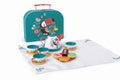 The HAPE Tea Time Playset for kids features a playful toucan design and includes a teal suitcase, a teapot, four cups with saucers, and a variety of pretend desserts, all arranged on a white cloth. Each item—the teapot, cups, saucers, and suitcase—is adorned with colorful bird and flower illustrations. This delightful set is perfect for fostering social skills during pretend play.
