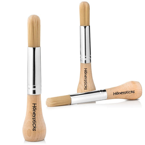 The Honeysticks My First Paint Brush Set - 3 pack is displayed on a white background. Each toddler paintbrush features a wooden, ergonomically designed handle and natural bristles, labeled with "Honeysticks My First Paintbrush" in black text. Two brushes are positioned upright, while one rests horizontally.