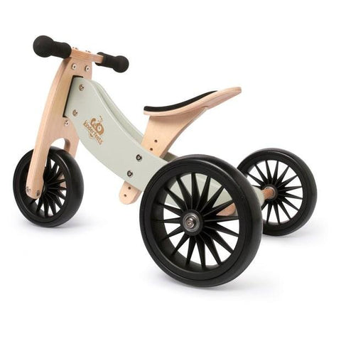 The Kinderboard Kinderfeet Tiny Tot Plus - Silver Sage is a wooden balance tricycle with a minimalist design, featuring black handle grips, black spoke-patterned wheels, and a light gray frame. The natural wood seat and handle add to its sleek and modern appearance, making it an ideal choice for young children learning to balance.