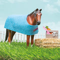 The "Klutz Wild About Horses" set by KLUTZ features a toy horse standing on grass with a blue blanket. It has a small brown heart-shaped marking on its forehead. Accompanying it is a bale of hay, along with a crate that contains carrots, a brush, and horseshoes—ideal for teaching horse care. In the background, there is a white picket fence under a blue sky dotted with clouds.