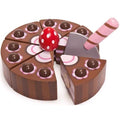 The *Le Toy Van Chocolate Gateau by LE TOY VAN features six wooden cake slices arranged in a circle, each adorned with a pink dollop and a brown sphere on top. The charming cake is beautifully decorated with brown frosting and pink accents. A red mushroom-shaped piece stands at the center, resembling an enchanting birthday cake toy, and a toy knife rests beside one of the slices.