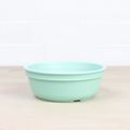 The Re-Play Bowl by REPLAY, a vibrant piece of tableware in light green, rests on a light wooden surface against a white tiled background. Featuring slightly tapered sides and a smooth finish, this round plastic bowl is made from recycled materials, making it safe for kids and perfect for any meal.