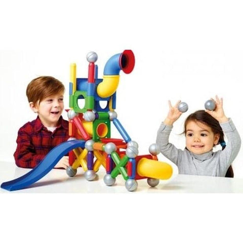 Two children are playing with a colorful SmartMax Mega Ball Run magnetic construction set. The 71-piece set from SmartMax includes tubes, connectors, and balls in various shapes and colors. One child, on the left, is smiling while the other, on the right, is lifting two balls in the air, also smiling.