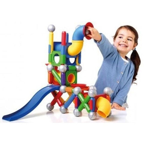 A smiling young girl wearing a blue shirt is joyfully engaged with the SmartMax Mega Ball Run (71 pc) by SmartMax. She plays with interconnected tubes, angles, and a slide, placing her hand into a yellow and red tube atop the vibrant construction set.